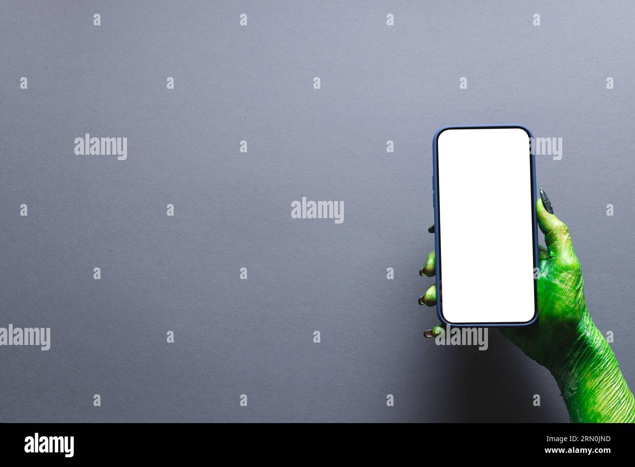 Vert monstre main tenant smartphone avec espace de copie sur fond gris Banque D'Images