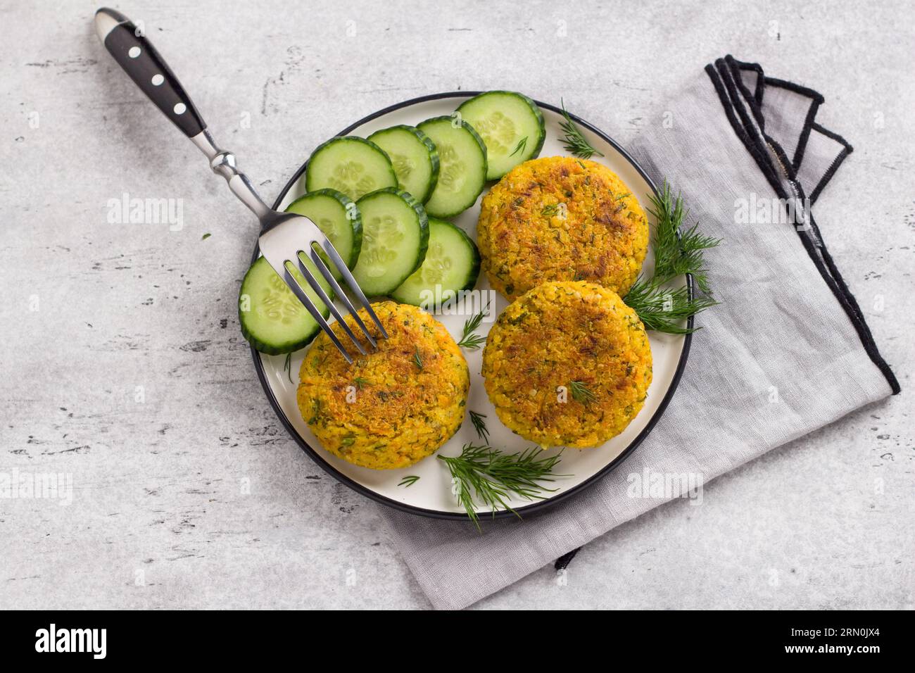 Délicieuses côtelettes de millet avec carottes et graines servies avec concombre et herbes sur un fond gris texturé, vue de dessus. Nourriture végétalienne maison. Banque D'Images