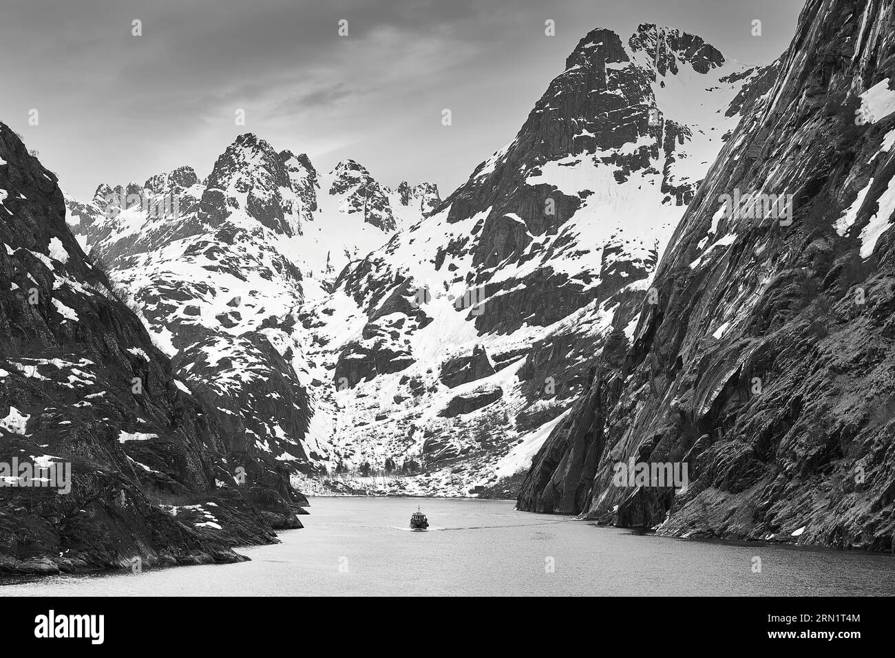 Photo en noir et blanc d'Un petit bateau touristique sortant du long Trollfjord de 2 km ou Trollfjorden entouré de montagnes de jusqu'à 1100m. Îles Lofoten Banque D'Images