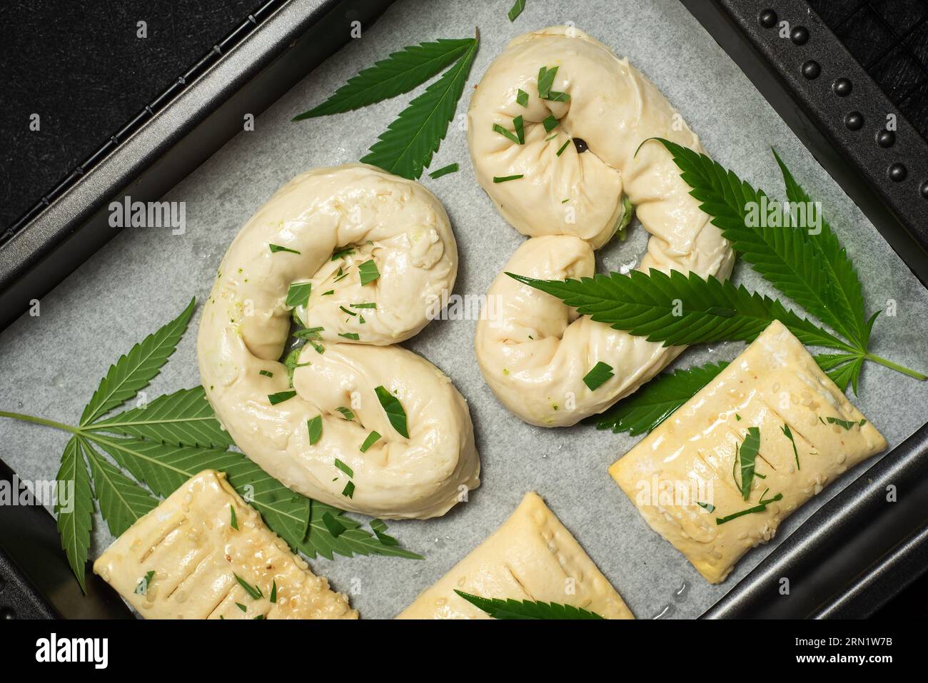 Nourriture avec cannabis. Tarte maison non cuite, décorée avec des feuilles de marijuana verte dans un plat allant au four sur marbre noir Banque D'Images