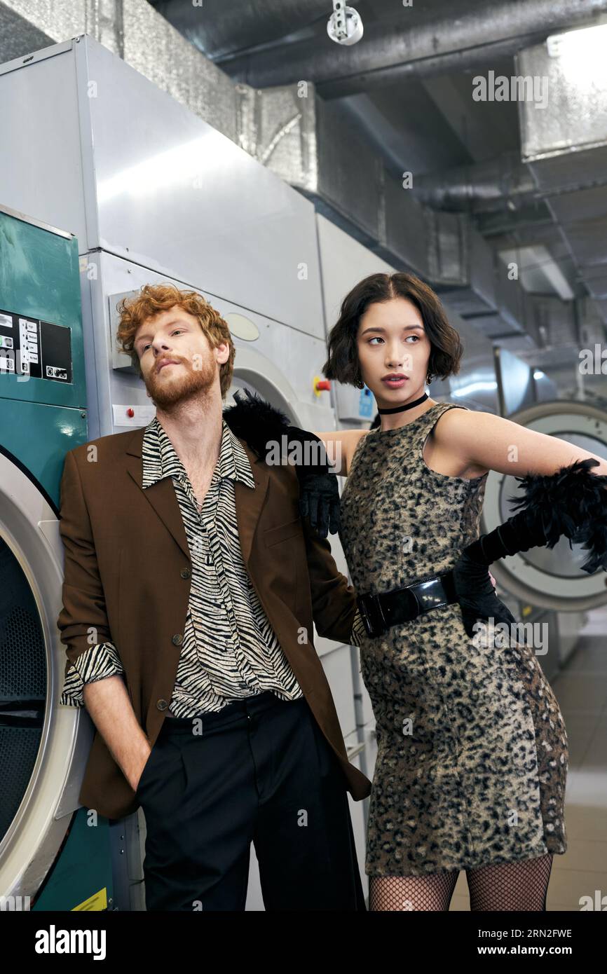 élégant jeune couple multiethnique posant près de la machine à laver dans la blanchisserie publique Banque D'Images