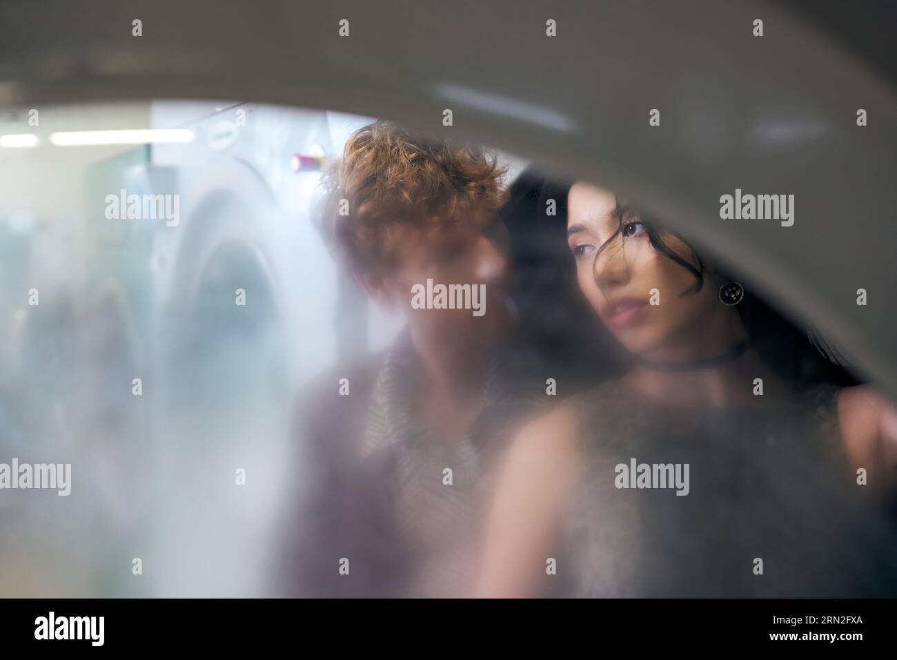 couple interracial dans des tenues élégantes debout derrière le verre de la machine à laver dans la buanderie de pièces Banque D'Images