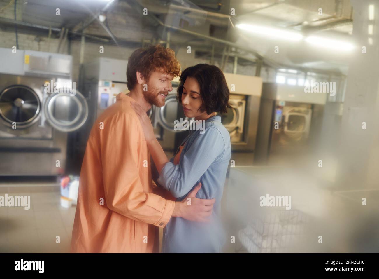 homme roux joyeux serrant une jeune petite amie asiatique dans une blanchisserie publique floue Banque D'Images