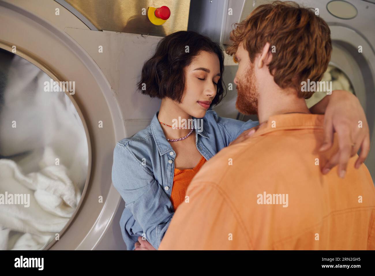 romantique jeune femme asiatique serrant copain rousse près de la machine à laver dans la blanchisserie publique Banque D'Images