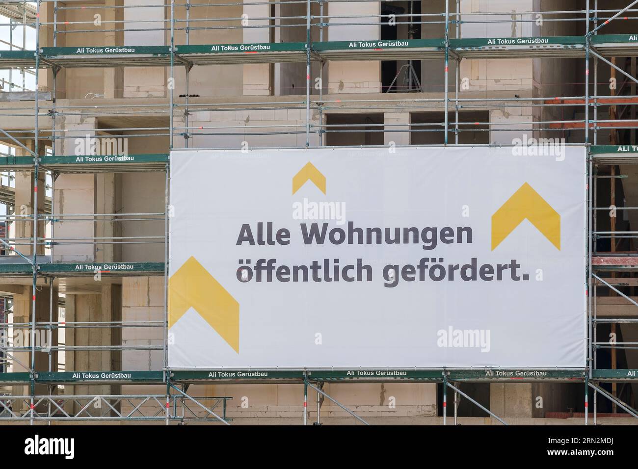 Chantier de construction où des appartements sont construits avec des échafaudages sur lesquels est accrochée une bannière indiquant que les appartements sont financés par des fonds publics. Banque D'Images