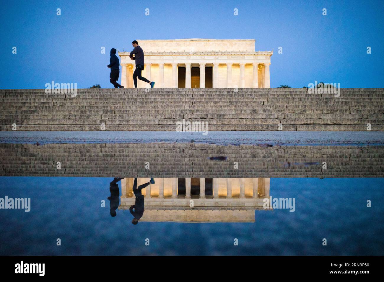Lincoln Memorial Joggers Reflection Washington DC // WASHINGTON DC — deux joggeurs courent devant le Lincoln Memorial avant l'aube, leurs silhouettes et le monument emblématique reflété dans une flaque sur les marches de la plaza. La scène capture l'interaction entre la vie quotidienne de la ville et ses monuments historiques, tandis que les amateurs d'exercices matinaux partagent l'espace avec l'un des monuments les plus vénérés d'Amérique avant l'arrivée des touristes de la journée. Banque D'Images