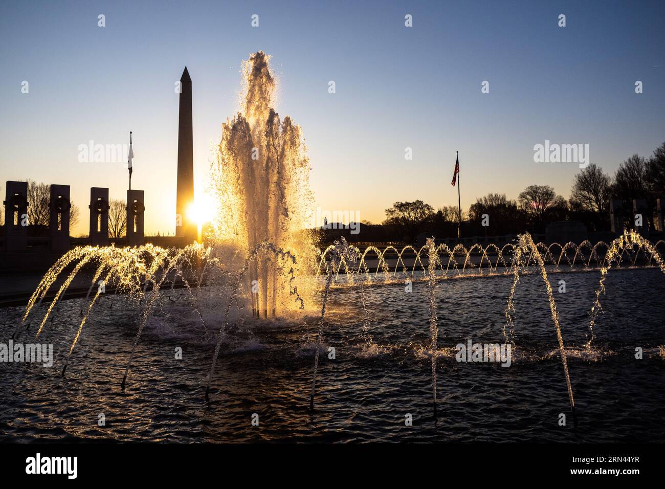 Fontaine du mémorial de la seconde Guerre mondiale Washington DC // WASHINGTON DC — la fontaine au centre du mémorial national de la seconde Guerre mondiale capte la lumière du soleil juste après le lever du soleil, avec le Washington Monument visible au loin. Le Rainbow Pool du mémorial sert de pièce maîtresse de la place de 7,4 acres (3 hectares) qui honore les 16 millions d'Américains qui ont servi pendant la IIe Guerre mondiale dédié en 2004, le mémorial comprend 56 piliers de granit représentant les états et territoires américains, disposés en demi-cercle autour de la fontaine cérémonielle. Banque D'Images