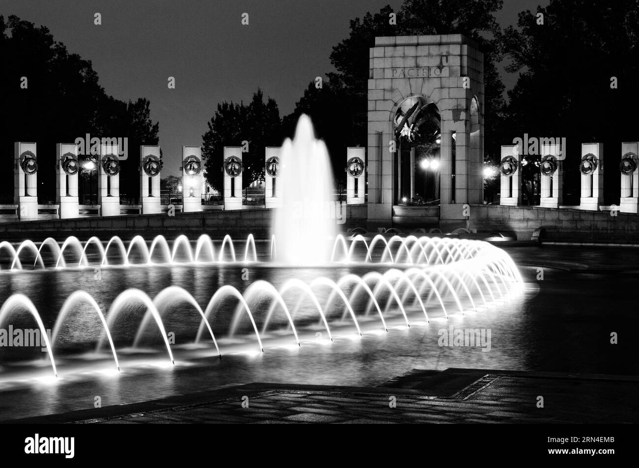 Fontaine commémorative de la seconde Guerre mondiale la nuit, Washington, D.C. photographie en noir et blanc montrant les jets d'eau illuminés et l'architecture environnante. Banque D'Images