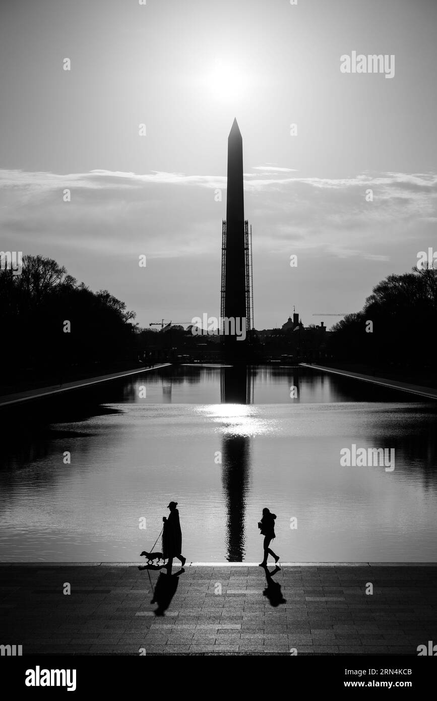 Washington Monument and Walkers silhouetted at Dawn, Washington, D.C. photographie en noir et blanc montre le reflet du monument dans la piscine réfléchissante, avec des piétons marchant le long du bord. Banque D'Images