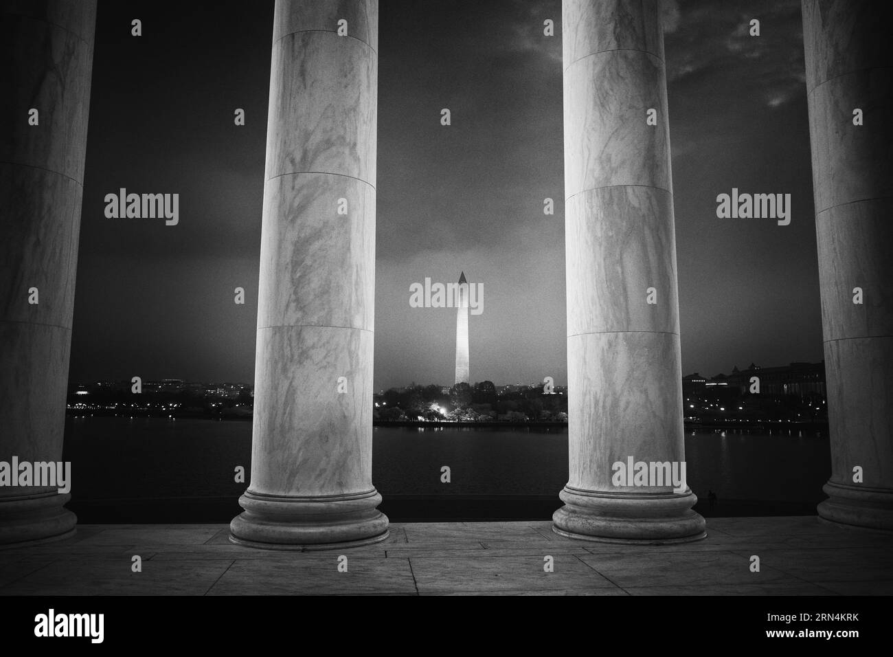 Monument Washington depuis les colonnes, Washington DC — Photo noir et blanc | Monument Washington depuis les colonnes, Washington, D.C. Photographie noir et blanc montrant l'obélisque encadré par des colonnes classiques et le paysage urbain reflété dans l'eau. Banque D'Images