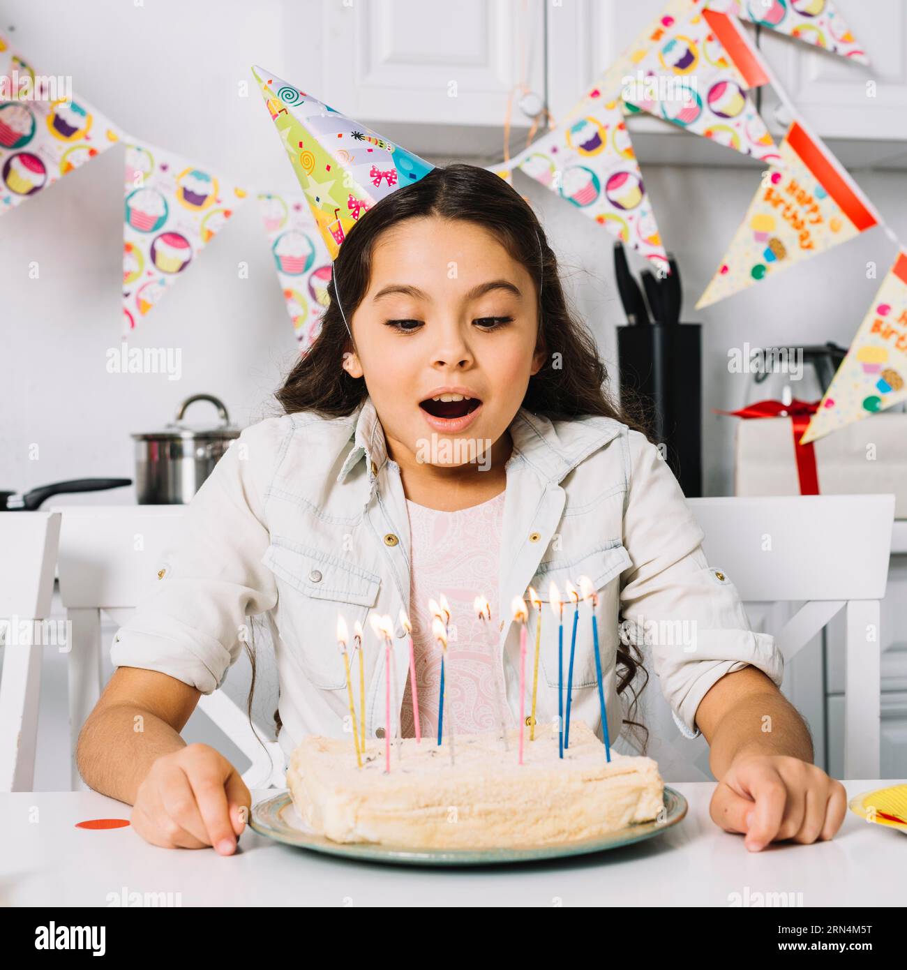 Fille d'anniversaire surprise soufflant un gâteau avec des bougies allumées Banque D'Images