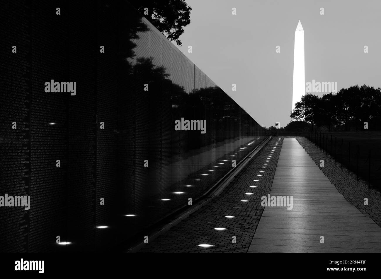 Mur commémoratif des vétérans du Vietnam, National Mall, Washington, D.C. photographie en noir et blanc montrant le mur poli reflétant le monument illuminé de Washington au loin. Banque D'Images