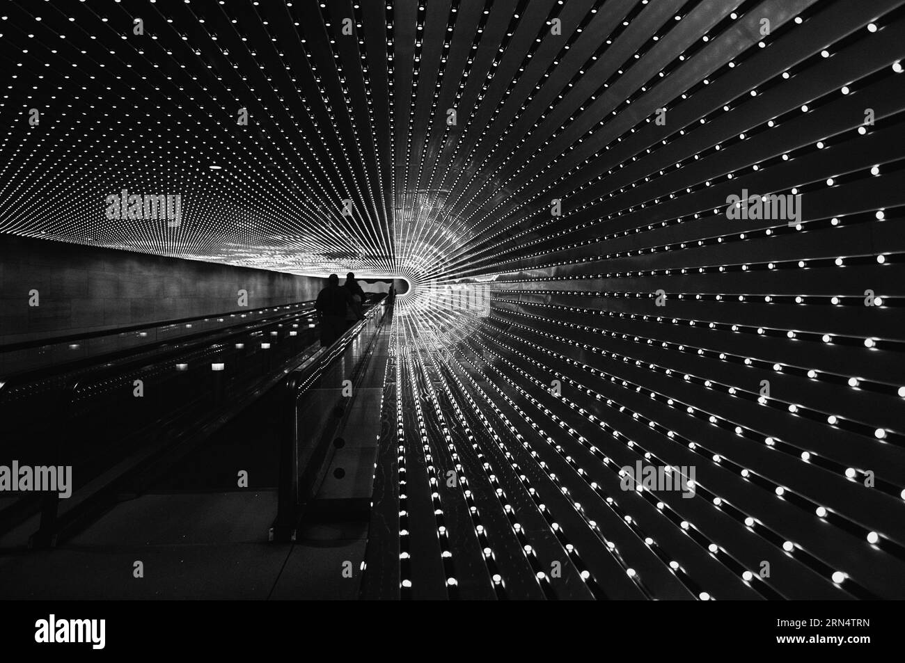Sculpture lumineuse Multiverse, National Gallery of Art, Washington, D.C. photographie en noir et blanc montrant les motifs lumineux rayonnants de l'œuvre au-dessus d'un escalier mécanique. Banque D'Images