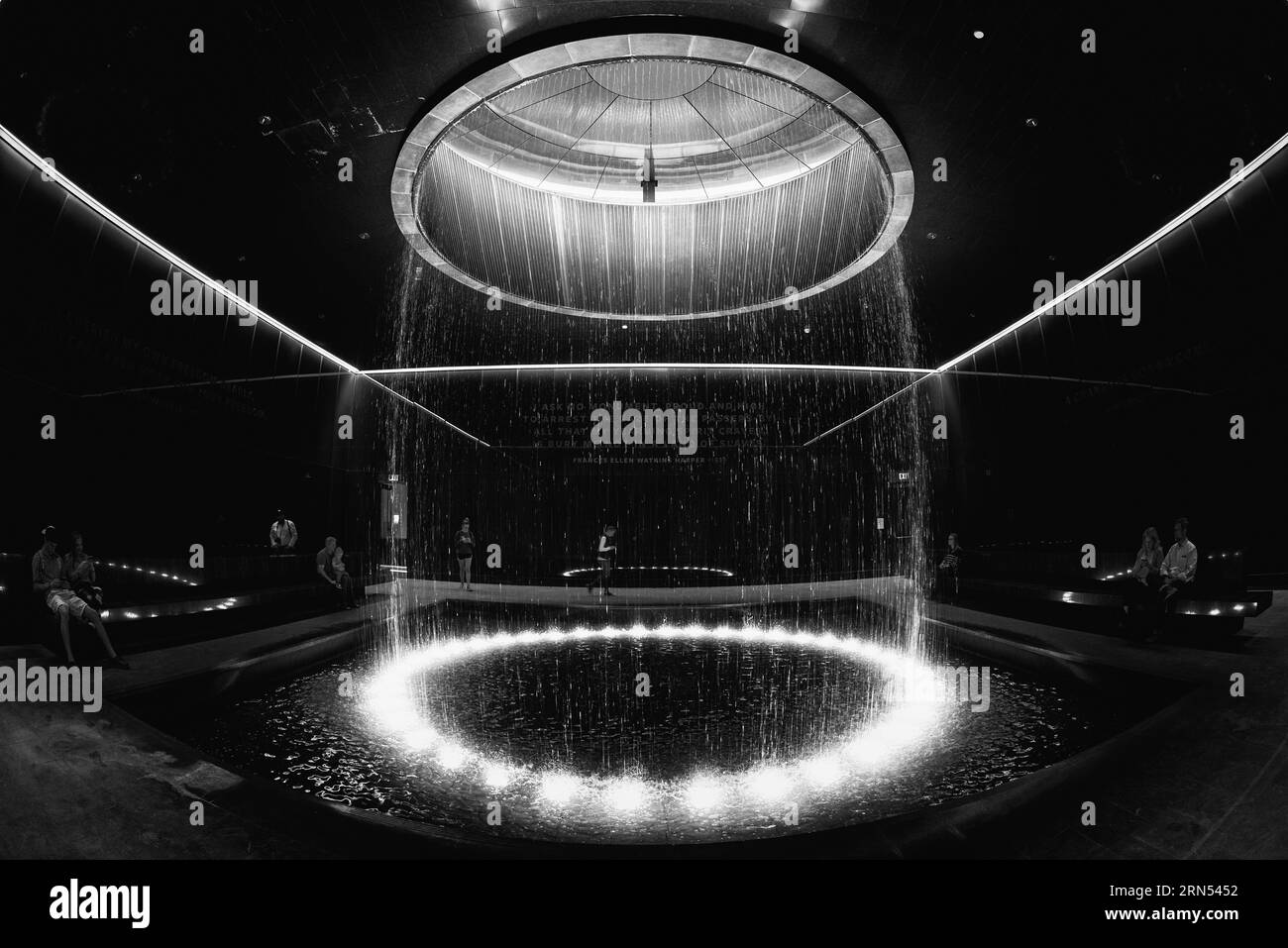 Fontaine au Legacy Museum, Montgomery Alabama — Photo noir et blanc | Fontaine du Legacy Museum, Montgomery, Alabama. Photographie en noir et blanc montrant la fontaine circulaire sous un anneau d'eau, avec des visiteurs observant depuis le périmètre. Banque D'Images