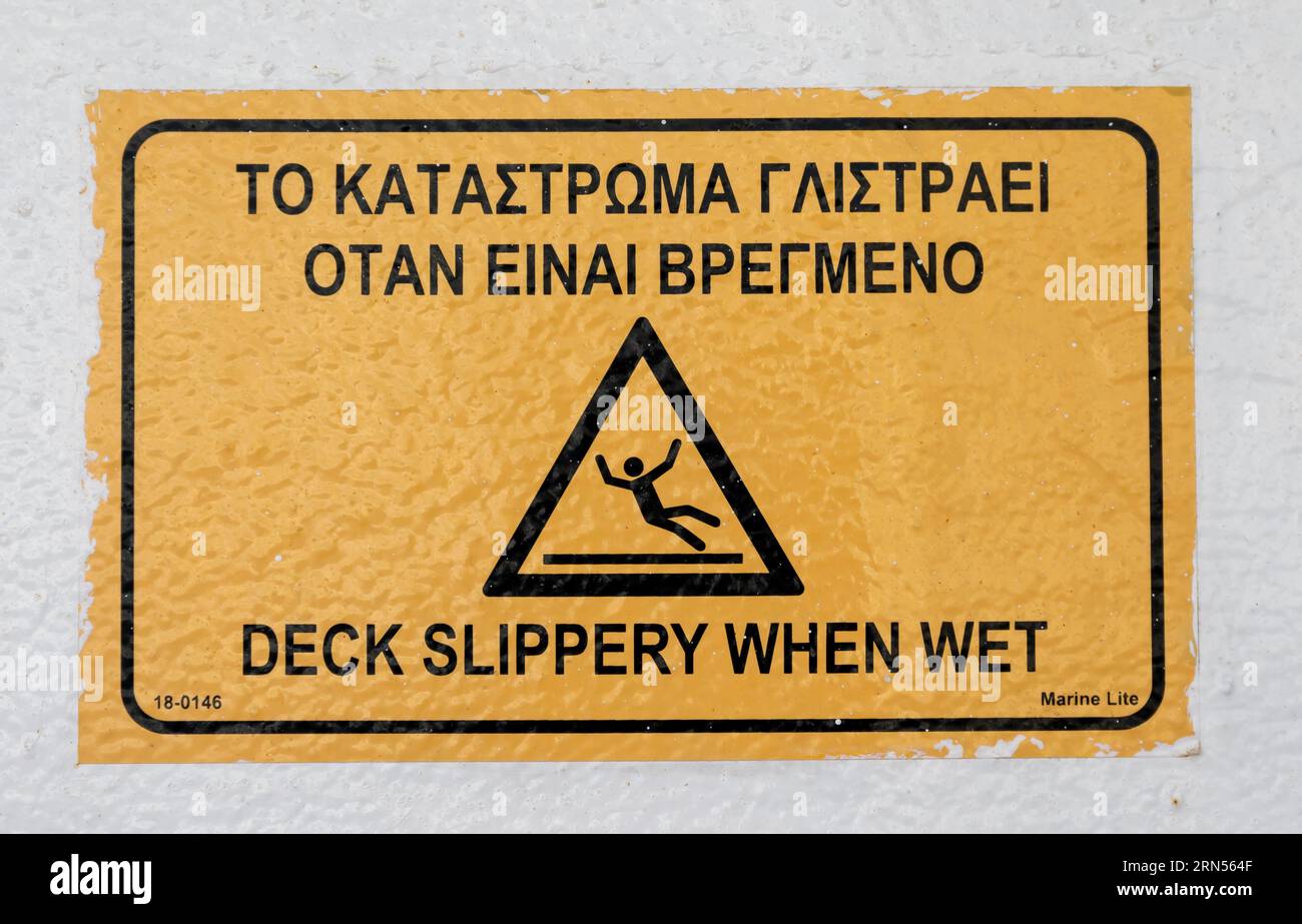 Panneau d'avertissement jaune, Pont glissant lorsqu'il est mouillé, à bord d'un ferry, en grec et en anglais, Cyclades, Grèce Banque D'Images