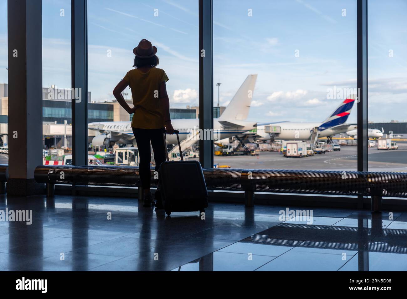 Silhouette de femme avec une valise dans le terminal de l'aéroport regardant les avions attendant le vol Banque D'Images