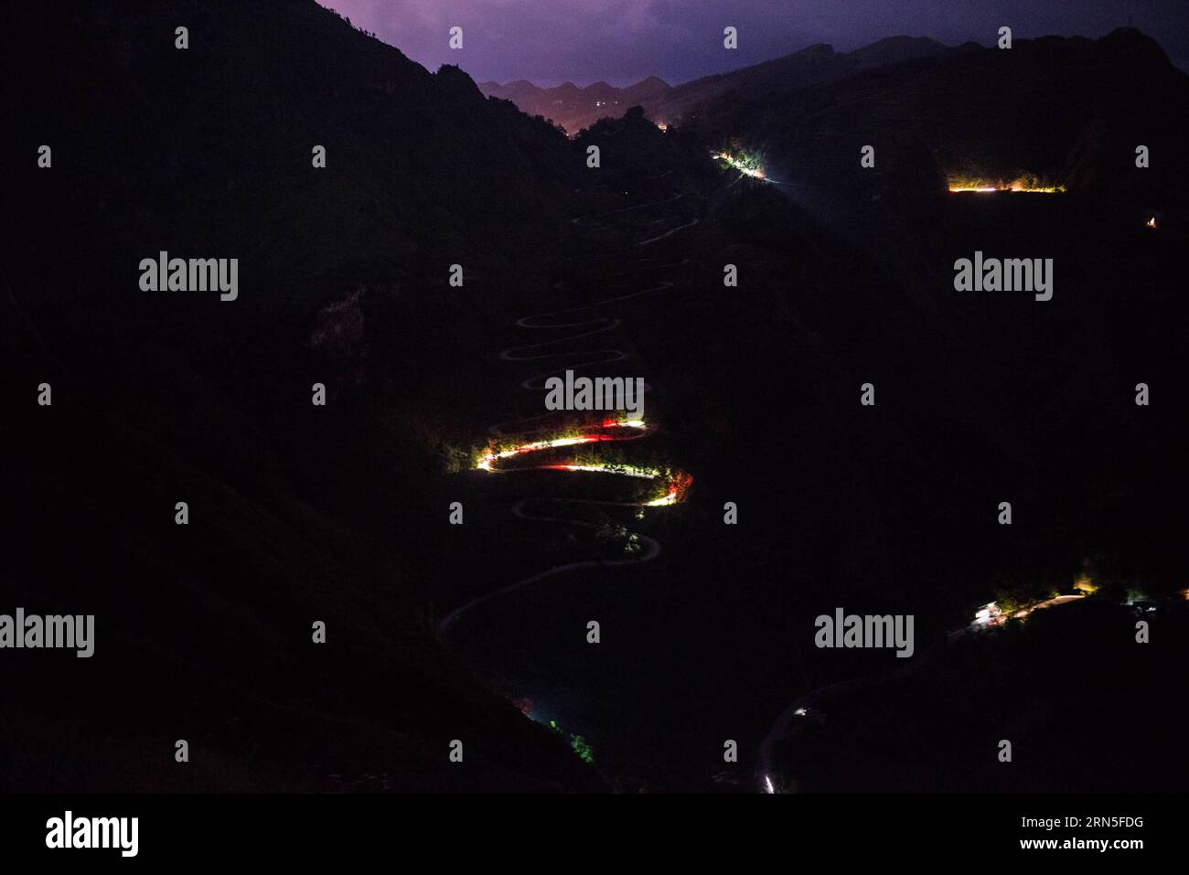 QINGLONG, le 24 juin 2015 -- cette photo à longue exposition prise par téléphone portable le 24 juin 2015 montre des traînées lumineuses de phares de voiture serpentant à travers un zigzag montagneux dans le comté de Qinglong, province du Guizhou au sud-ouest de la Chine. Le zigzag montagneux, également appelé 24-zig, qui est une section de la célèbre route de Stilwell, a vu plus de 2000 camions entièrement chargés de fournitures militaires passer chaque jour pendant la Seconde Guerre mondiale La route sinueuse de montagne a été terminée en 1935. En 1942, le corps du génie américain l'a rénové pour en faire une partie de la route Yunnan-Guizhou, une section de la route de Ledo, ou la route de Stilwell. Banque D'Images