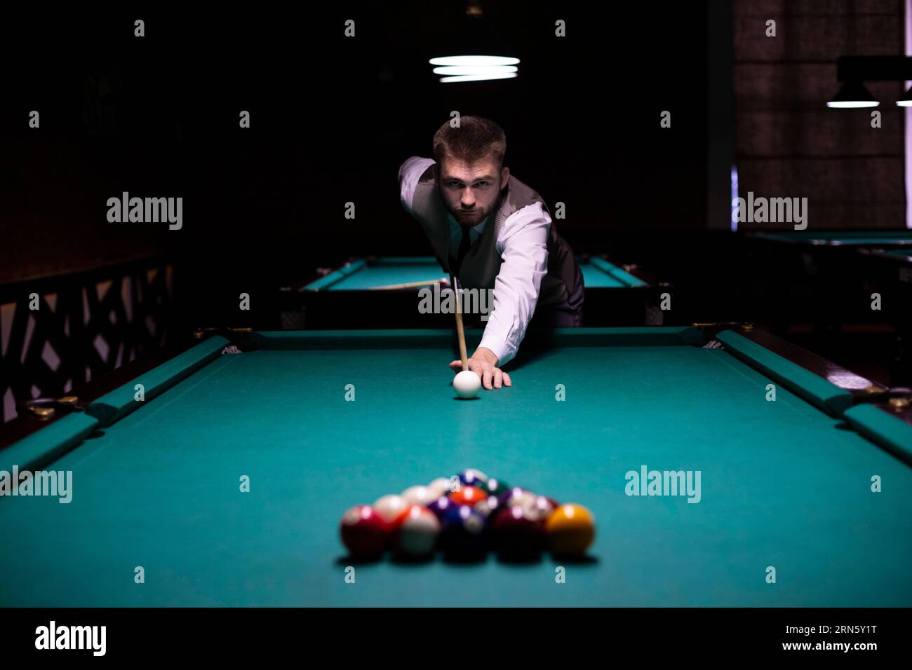 Gars à tir moyen avec queue de billard frappant une balle blanche Banque D'Images