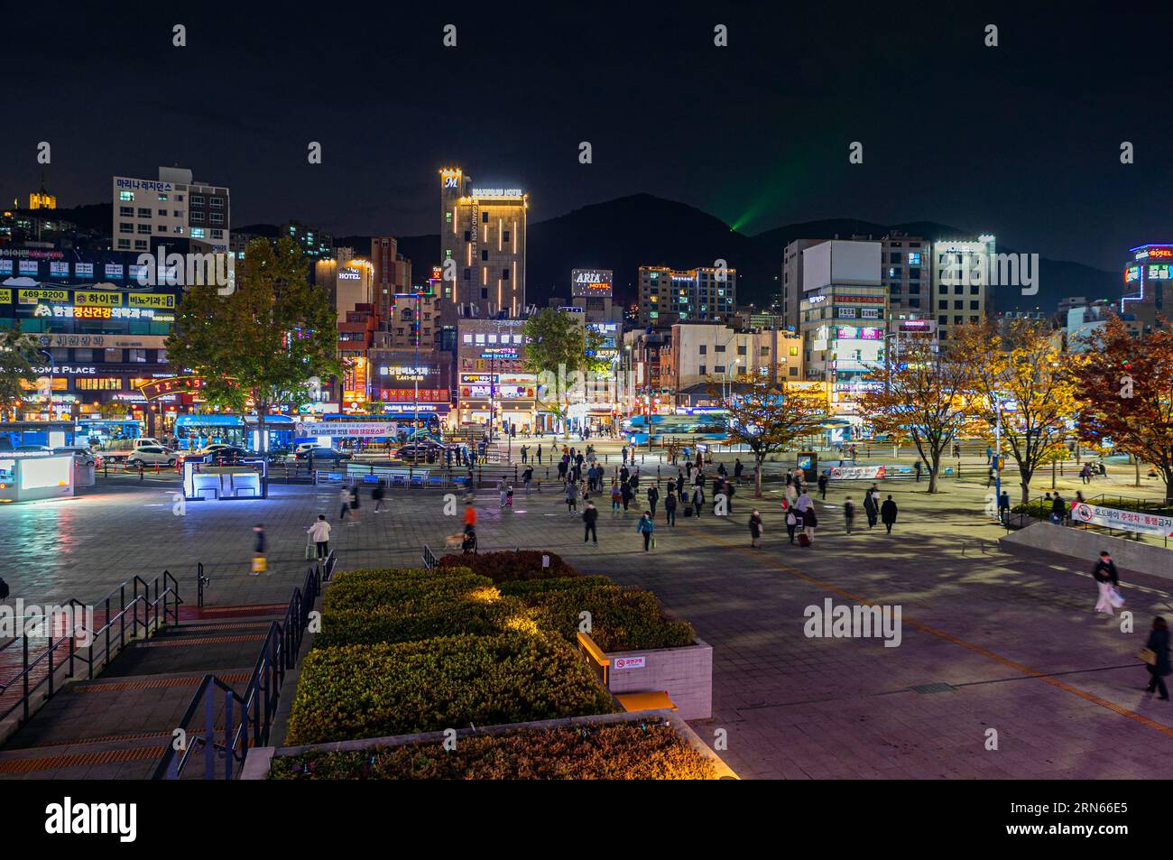 Parvis de la gare, gratte-ciel et boutiques avec enseignes au néon, montagnes derrière, shot de nuit, Busan, province de Gyeongsangnam-do Banque D'Images