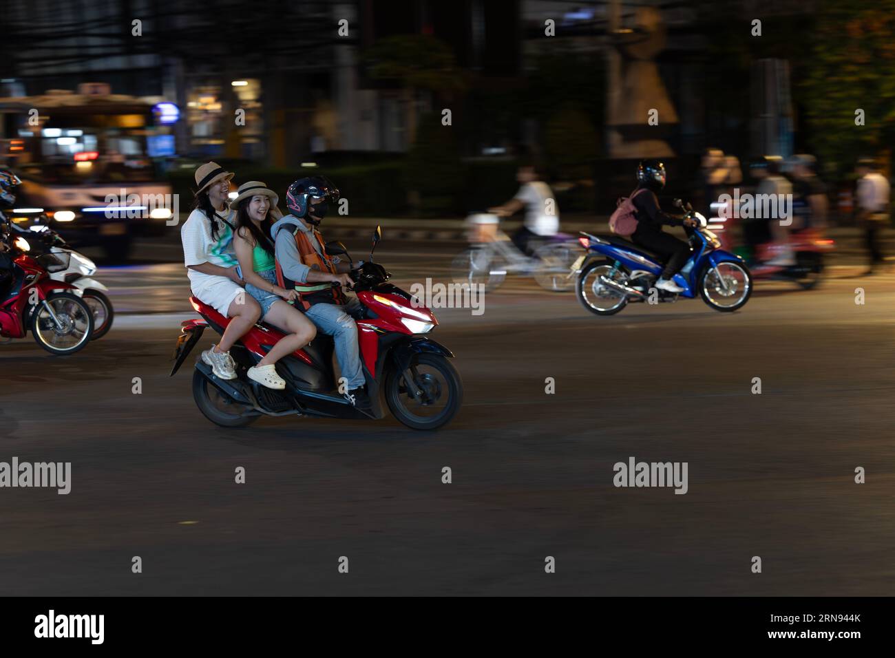 Deux filles heureuses avec des chapeaux montent à l'arrière d'un taxi moto à bangkok la nuit. Banque D'Images