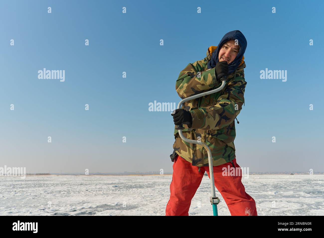 Un homme asiatique habillé chaleureusement perce un trou dans la glace sur fi d'hiver Banque D'Images