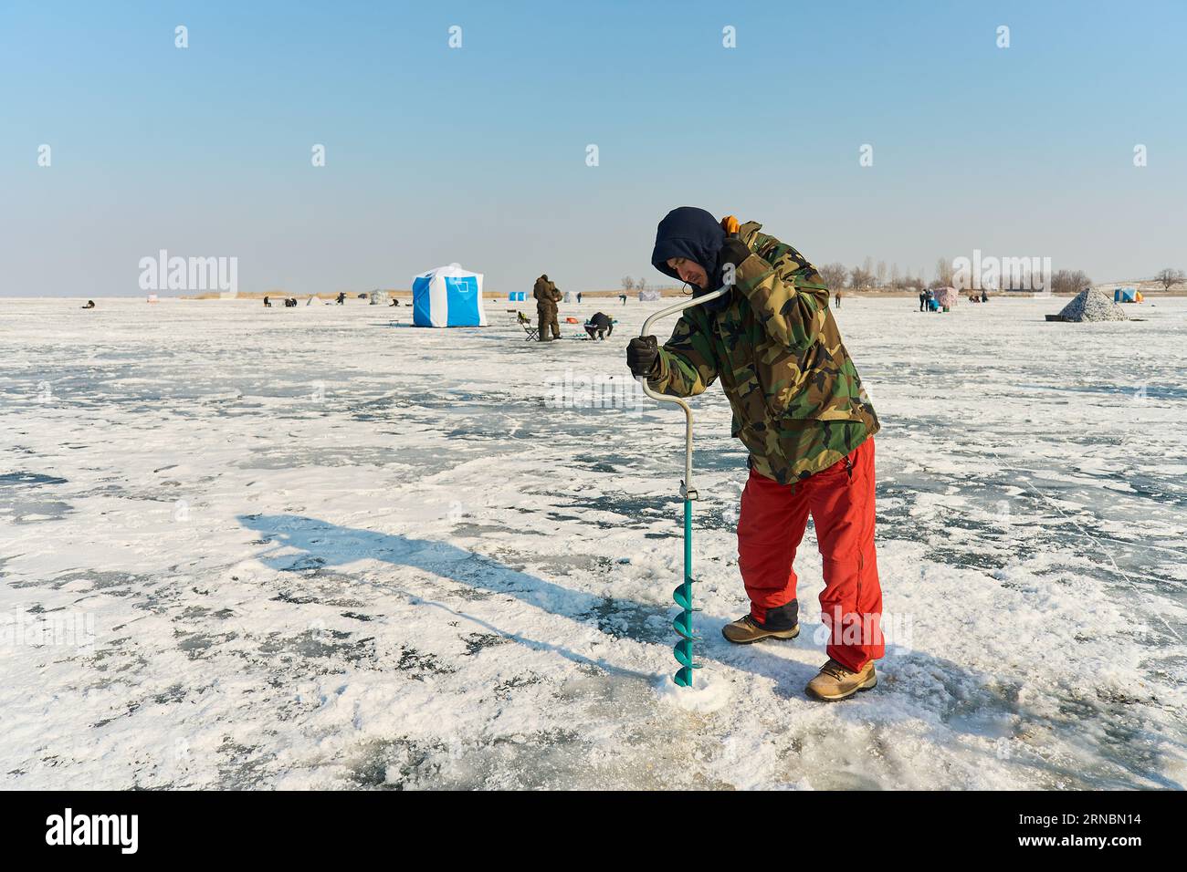 Un homme asiatique habillé chaleureusement perce un trou dans la glace sur fi d'hiver Banque D'Images