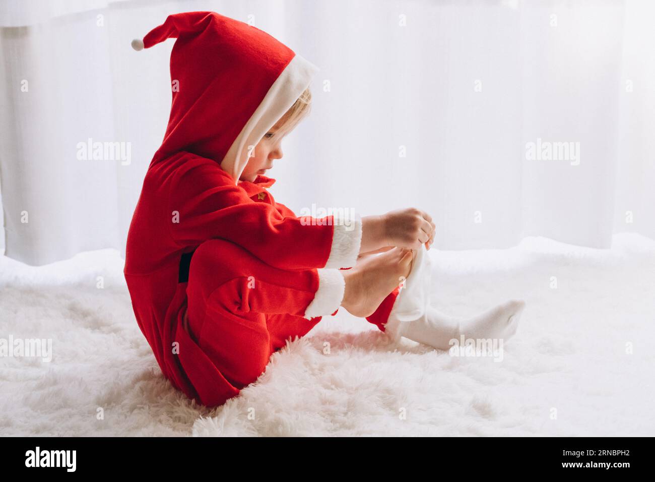 Enfant habillé comme le Père Noël s'assoit et met des chaussettes Banque D'Images