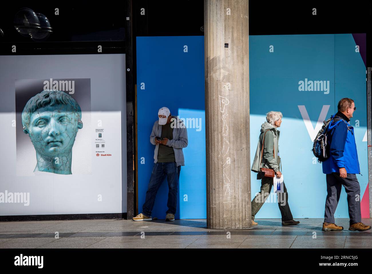 Un homme se tient devant le musée romano-germanique à côté d'une affiche avec une photo de la tête portrait d'Auguste, passants, Cologne, Allemagne. ein M. Banque D'Images