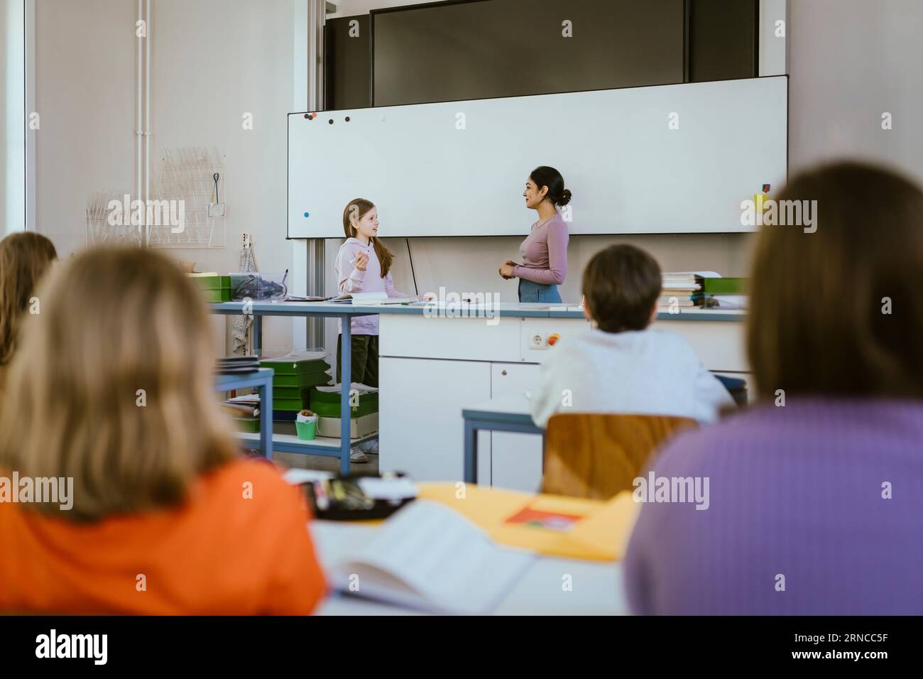Enseignant debout et parlant avec une étudiante près du tableau blanc dans la salle de classe Banque D'Images
