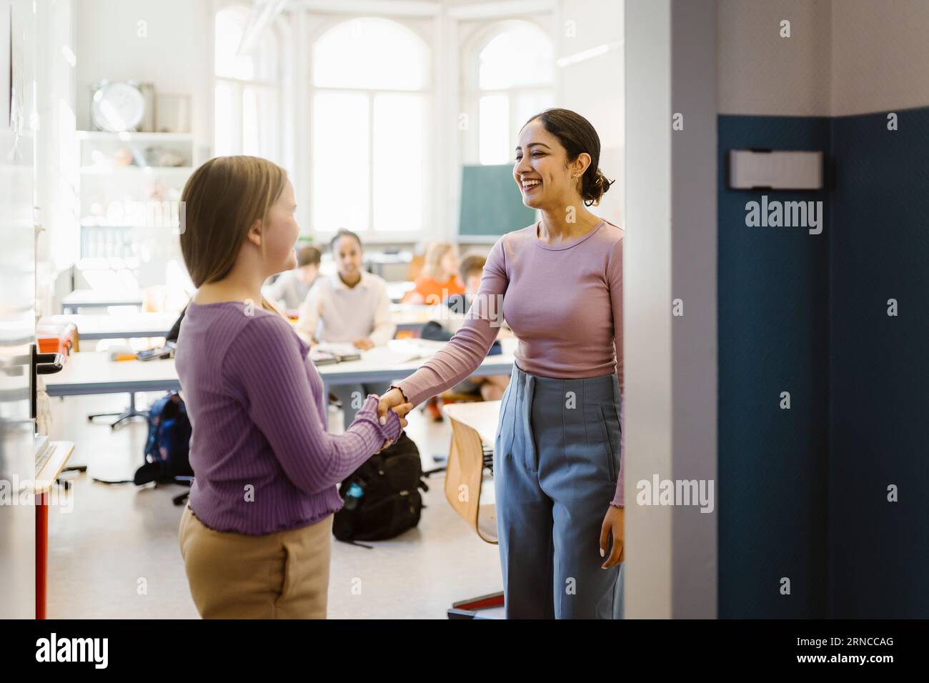 Enseignante souriante faisant une poignée de main avec l'élève debout dans la salle de classe Banque D'Images