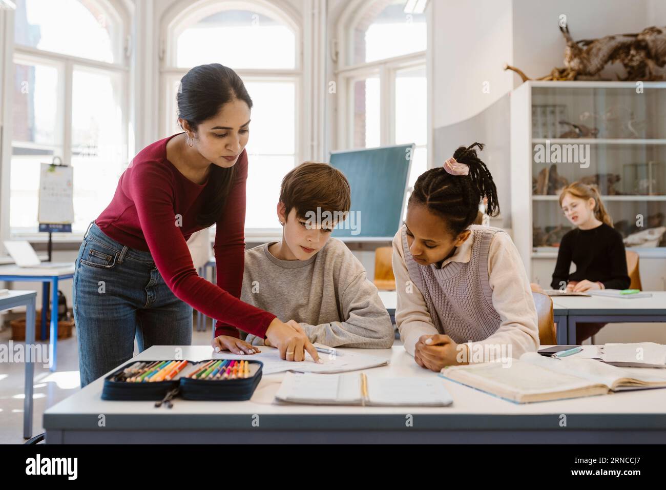 Enseignant expliquant les élèves masculins et féminins assis au bureau dans la salle de classe Banque D'Images