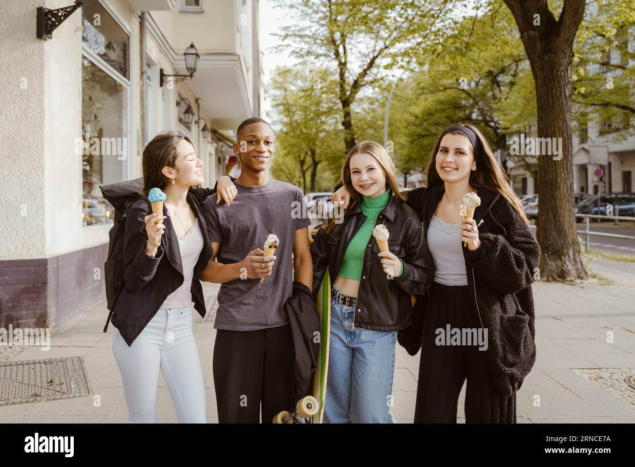 Portrait de jeunes amis souriants mangeant des glaces sur le trottoir Banque D'Images