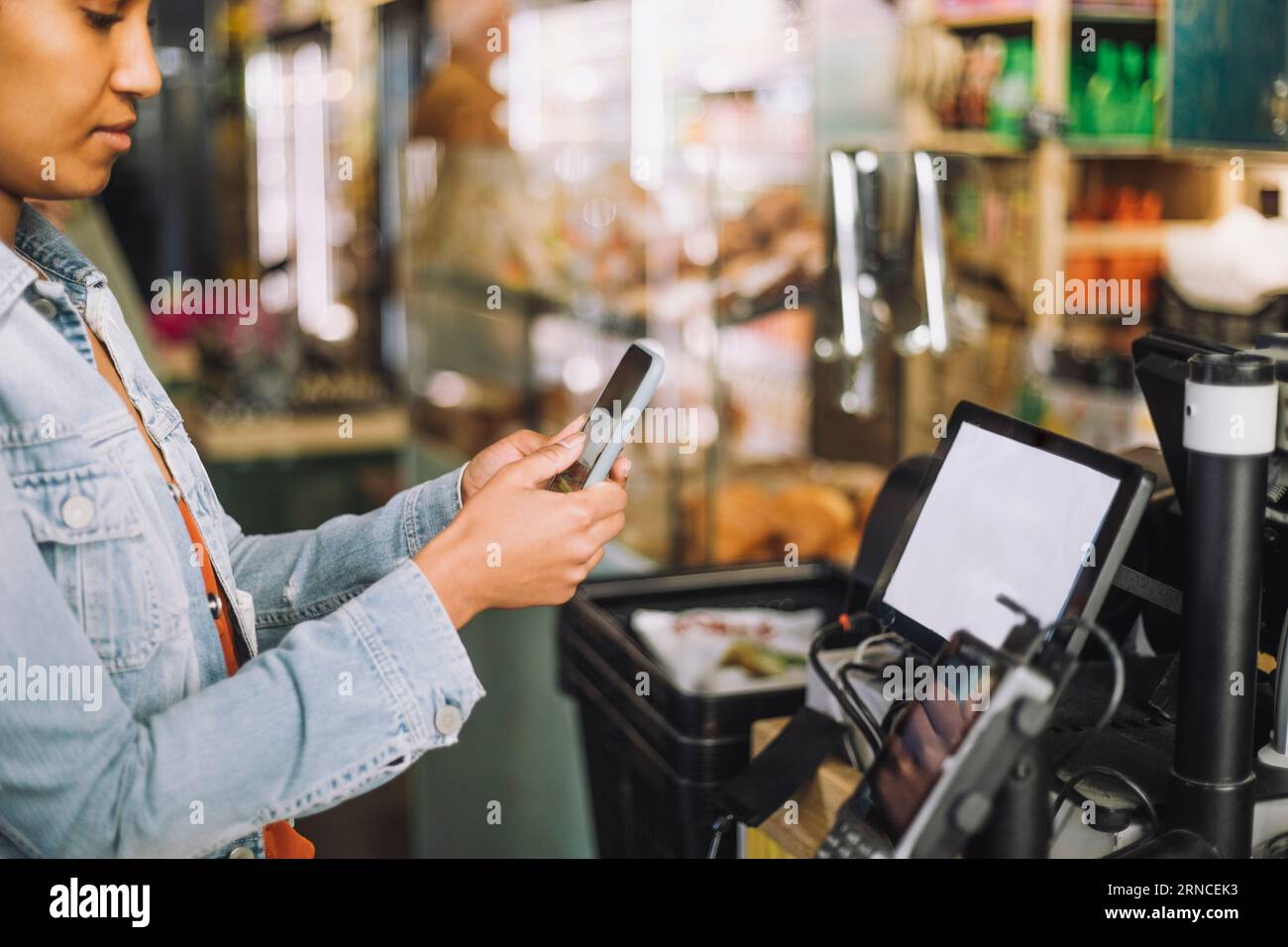 Femme utilisant un téléphone intelligent tout en scannant le code QR pour le paiement à la caisse du magasin Banque D'Images