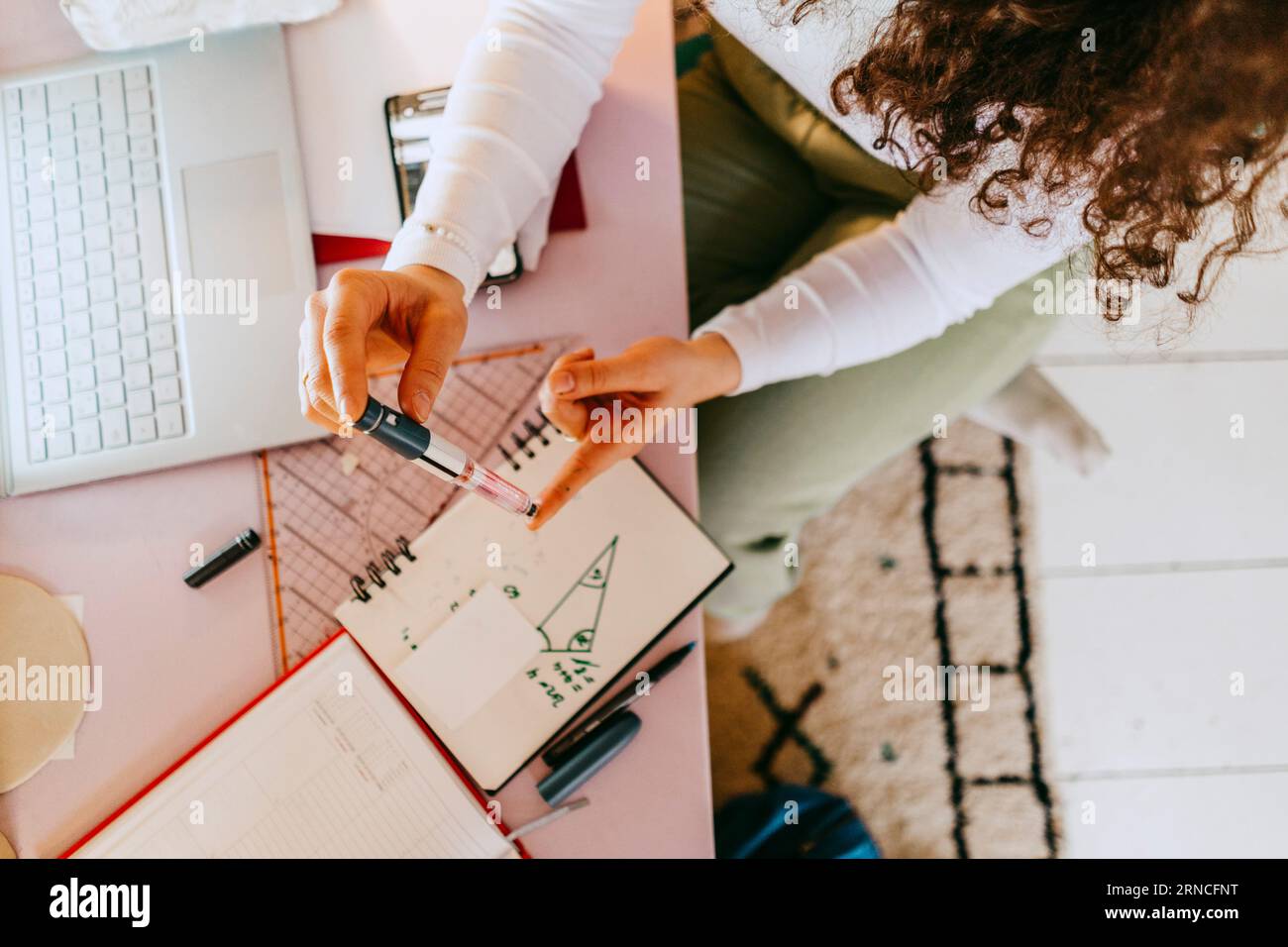 Vue à grand angle d'une femme utilisant un glucomètre tout en faisant ses devoirs à table Banque D'Images