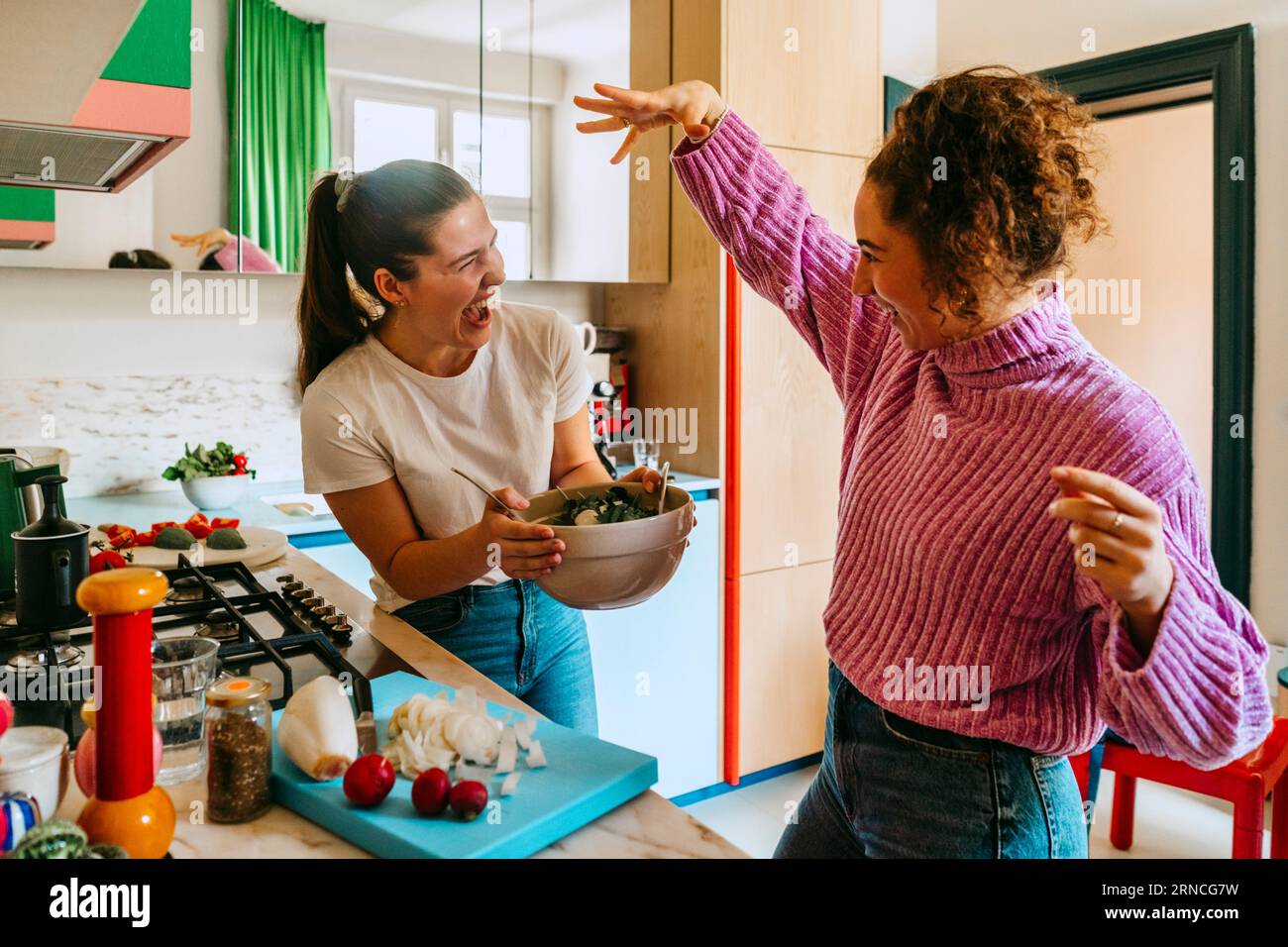 Jeunes amies joueuses appréciant tout en faisant de la salade dans la cuisine à la maison Banque D'Images