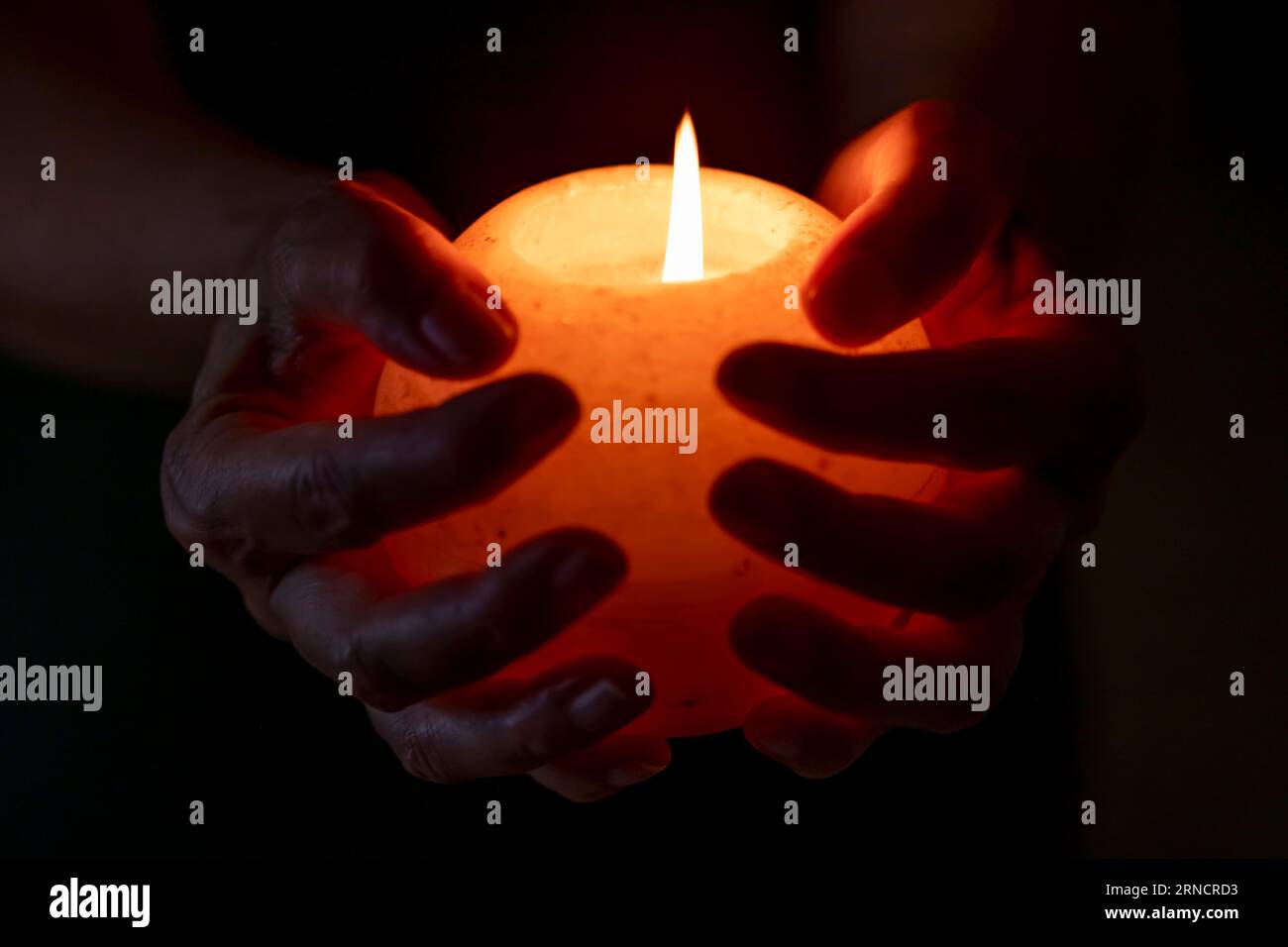 Female hands hold a round white candle with a burning flame Banque D'Images