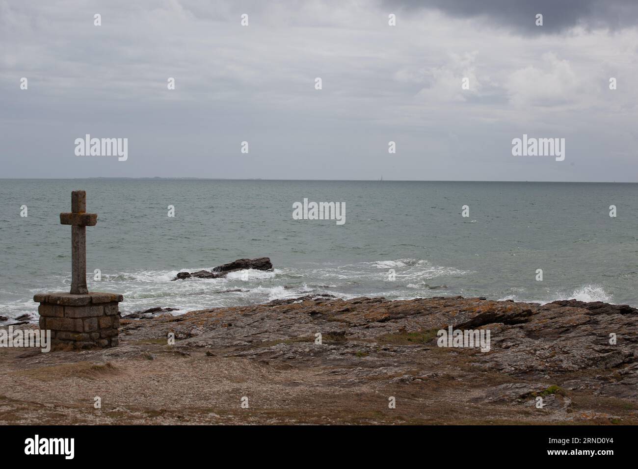 La côte atlantique découpée par mauvais temps avec une croix catholique en granit au premier plan. Banque D'Images