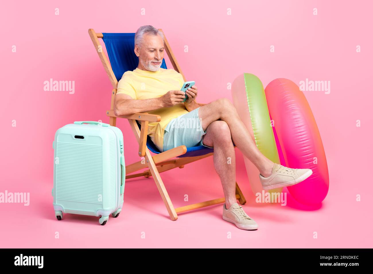 Photo pleine longueur de relaxation vieil homme pension de navigation téléphone envoyer ses photos famille couchée lit de soleil isolé sur fond de couleur rose Banque D'Images