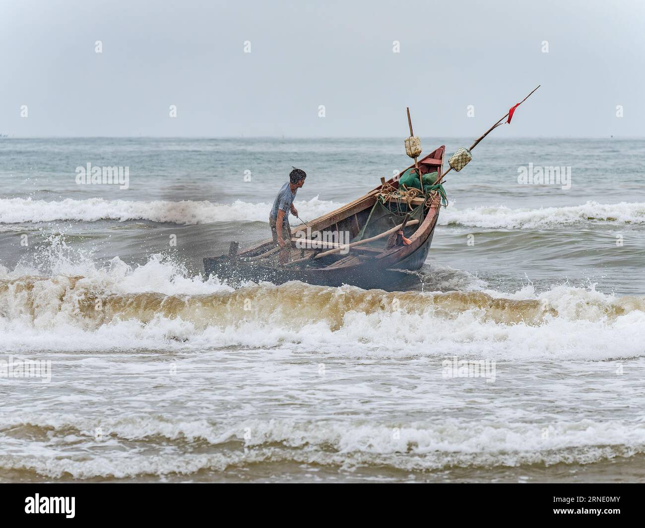 Pêcheur lançant son bateau contre le vent et les hautes vagues à Sam son Beach, Thanh Hoa, Vietnam Banque D'Images