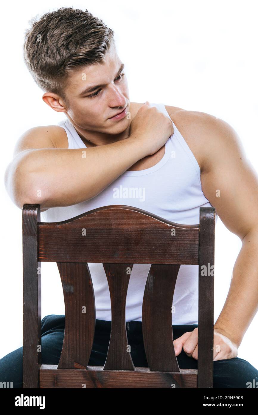 homme avec muscle et chemise s'asseoir sur la chaise et regarder sur le côté tout en pensant à quelque chose de sérieux Banque D'Images