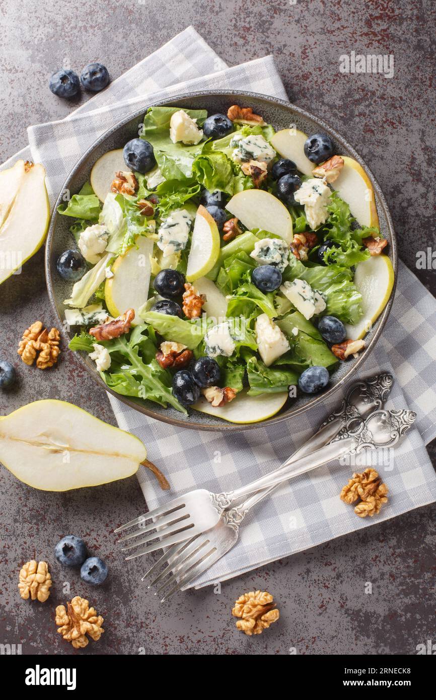 Salade d'automne vitaminée avec bleuets, laitue, fromage gorgonzola, noix et poire gros plan dans une assiette sur la table. Vue verticale de dessus Banque D'Images