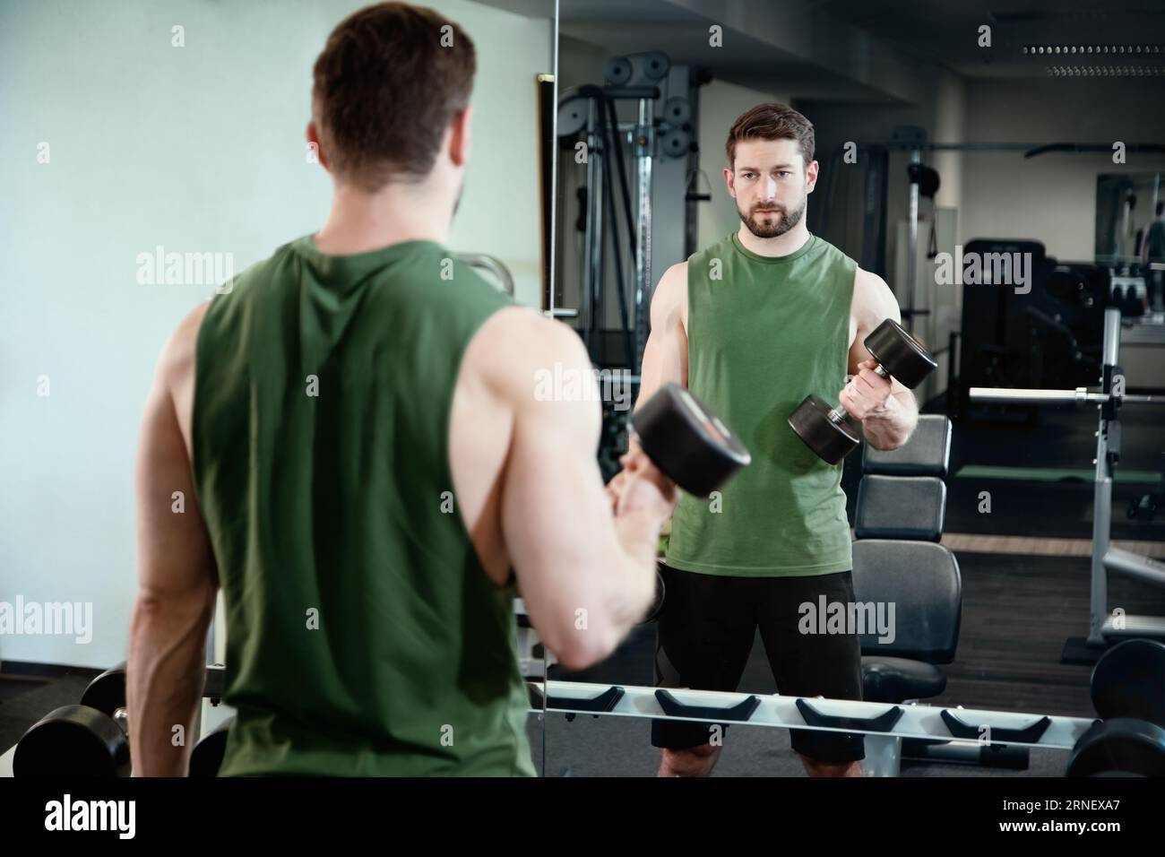 soulevez des haltères à la salle de gym tout en regardant le miroir pour contrôler la bonne séance d'entraînement et admirer sa propre apparence Banque D'Images