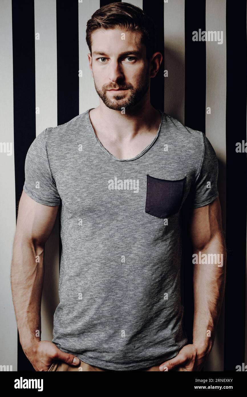 homme bien entraîné debout à côté du mur avec les mains dans les poches regarder la caméra avec l'expression du visage sérieux et neutre Banque D'Images