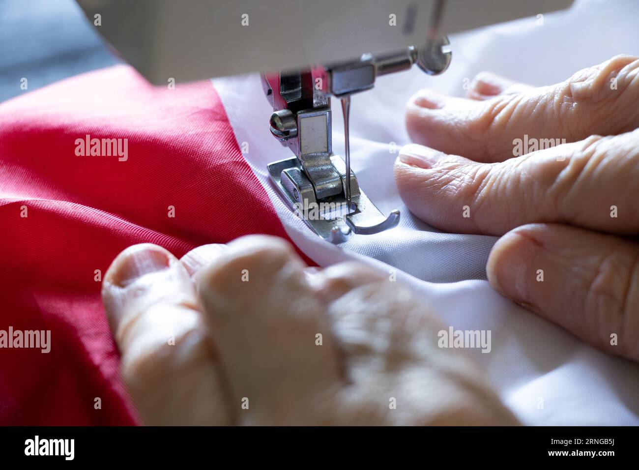 Les mains d'une femme âgée cousent le drapeau de la Pologne sur une machine à coudre, la production et le travail Banque D'Images