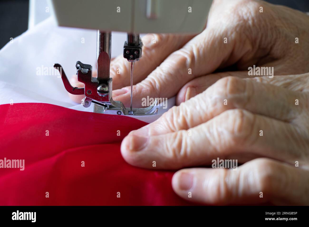 Les mains d'une femme âgée cousent le drapeau de la Pologne sur une machine à coudre, la production et le travail Banque D'Images