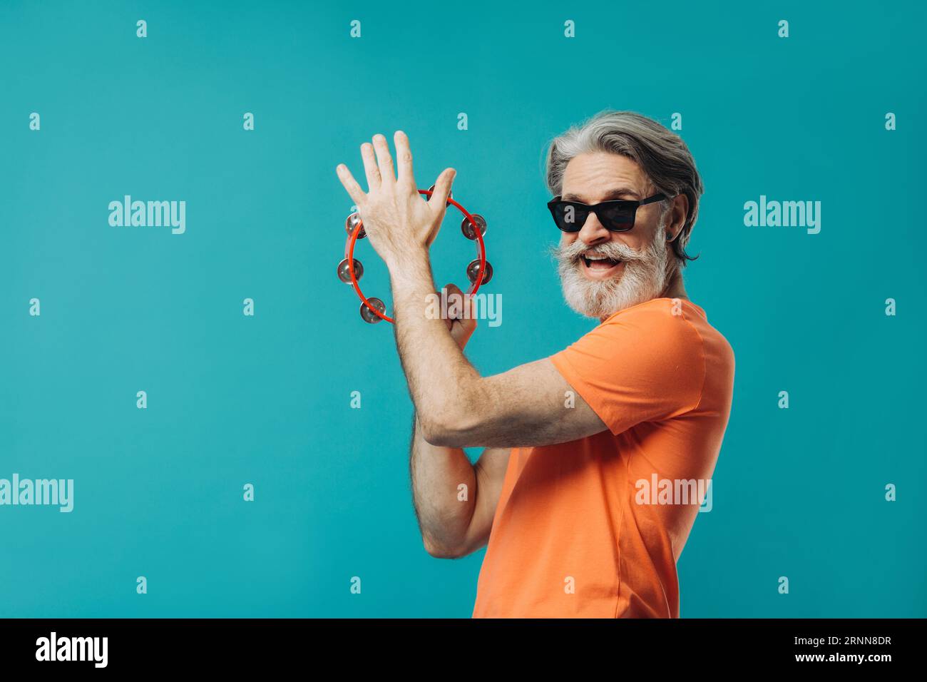 Un vieil homme barbu aux cheveux gris danse avec un tambourin. Photo de studio sur un fond coloré. Banque D'Images