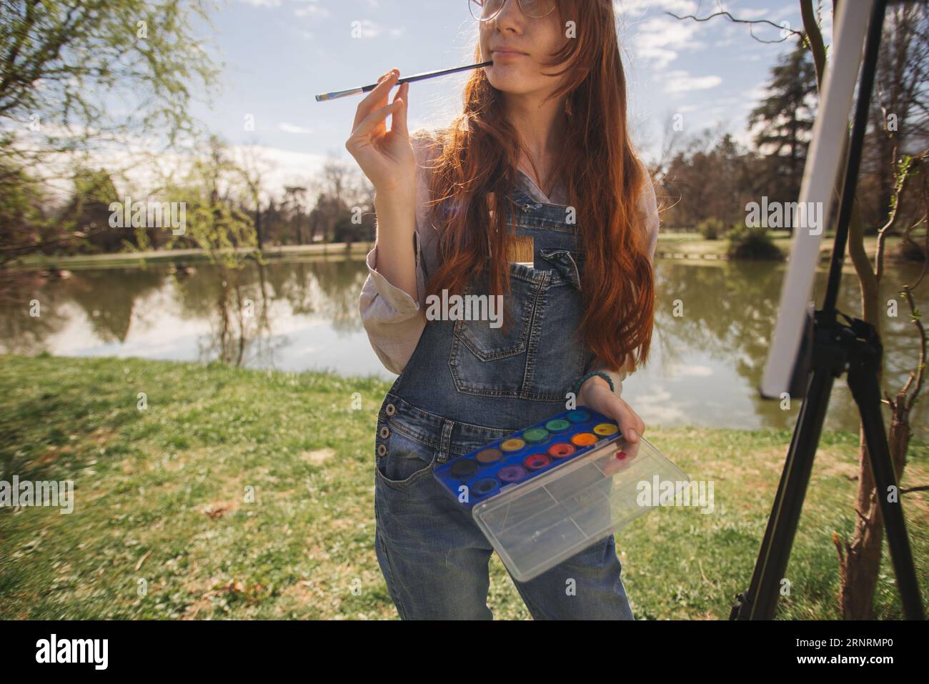 Gros plan de femme de gingembre tenant la palette de couleurs et un pinceau tout en se tenant au parc près du lac Banque D'Images