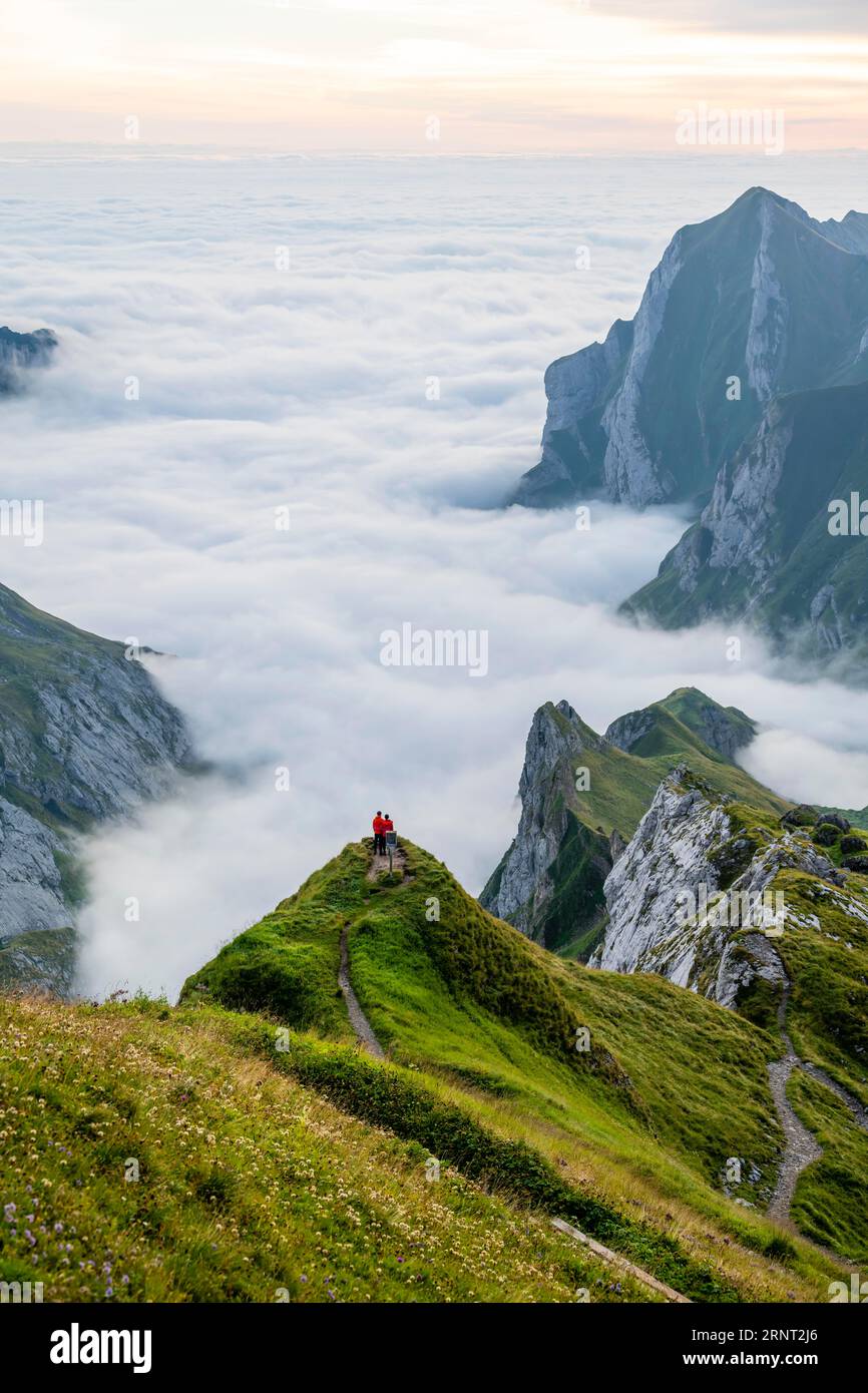 Deux randonneurs profitant de la vue sur les montagnes de Saentis dans la vallée de Meglisalp au lever du soleil, haut brouillard dans la vallée, Saentis, Appenzell Banque D'Images