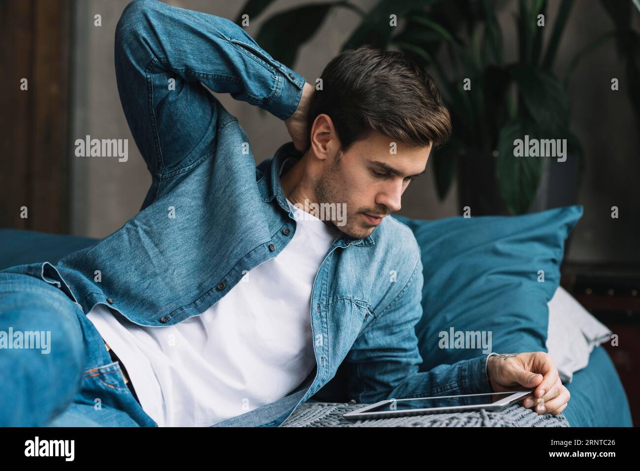 Jeune homme couché au lit regardant tablette numérique Banque D'Images
