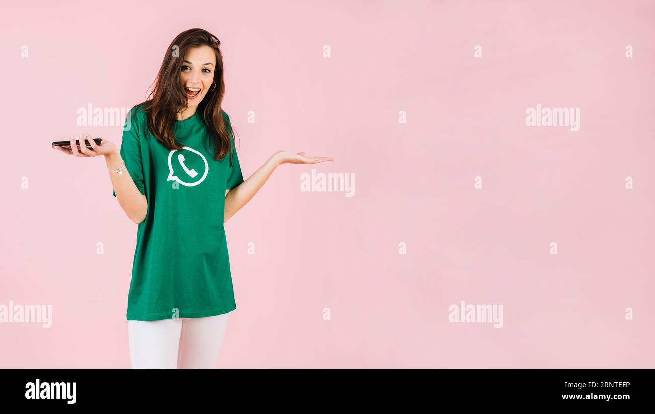 Femme heureuse avec smartphone haussant la toile de fond rose Banque D'Images